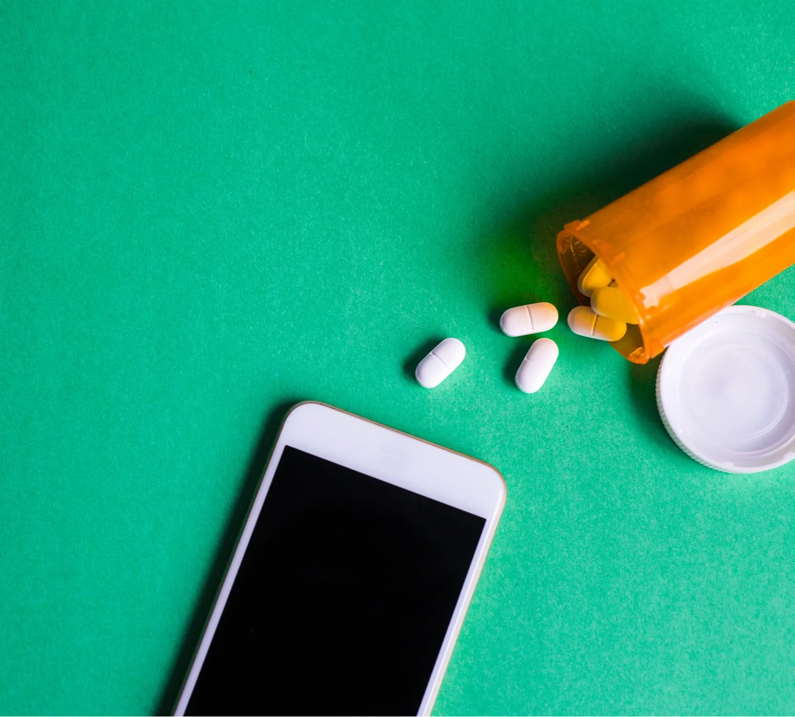 A smartphone next to prescription pills spilling from a bottle, symbolizing Forty Health’s telehealth services for men’s health, including hormone therapy, weight loss, and wellness treatments.