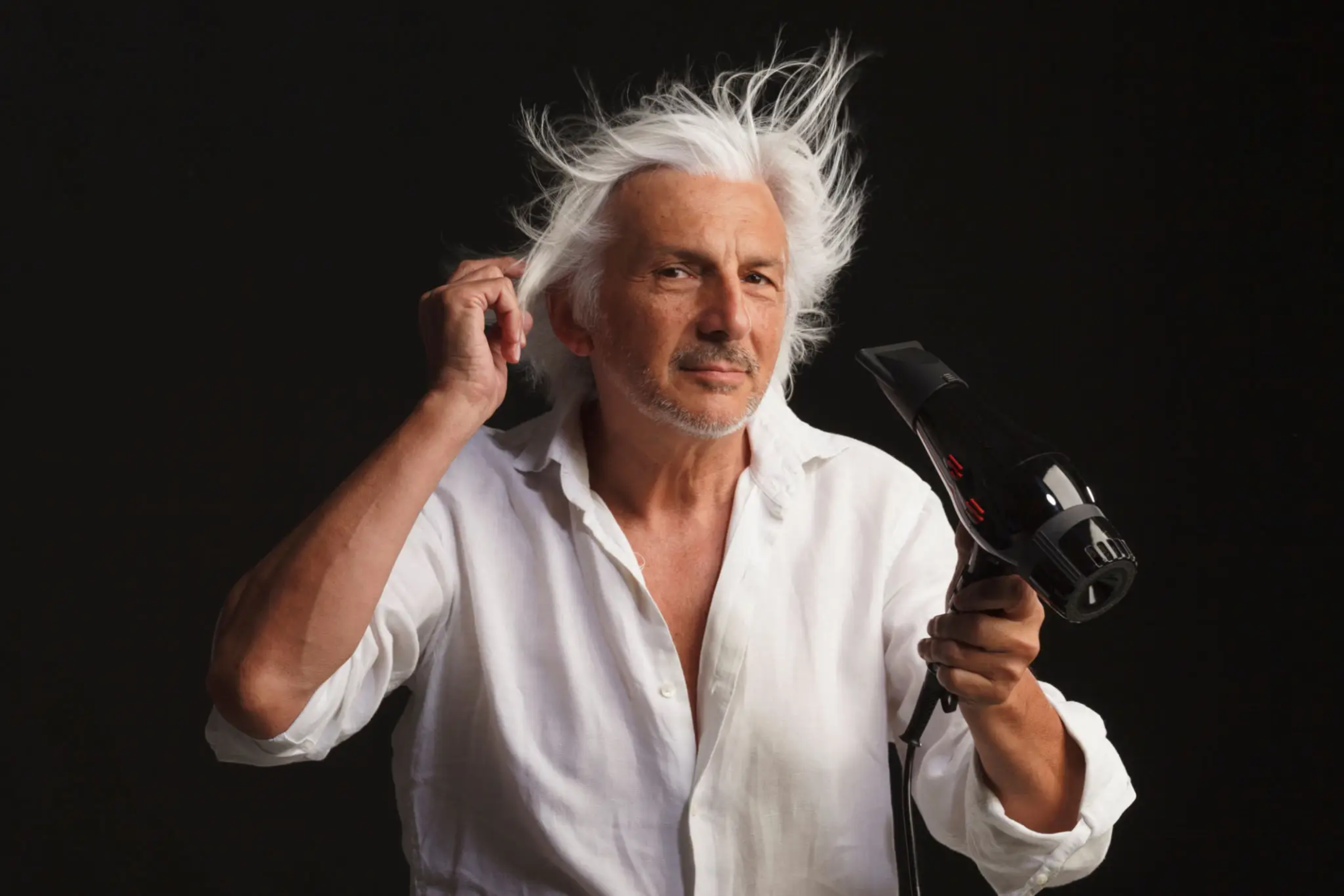 Man with white hair using a hair dryer against a black background