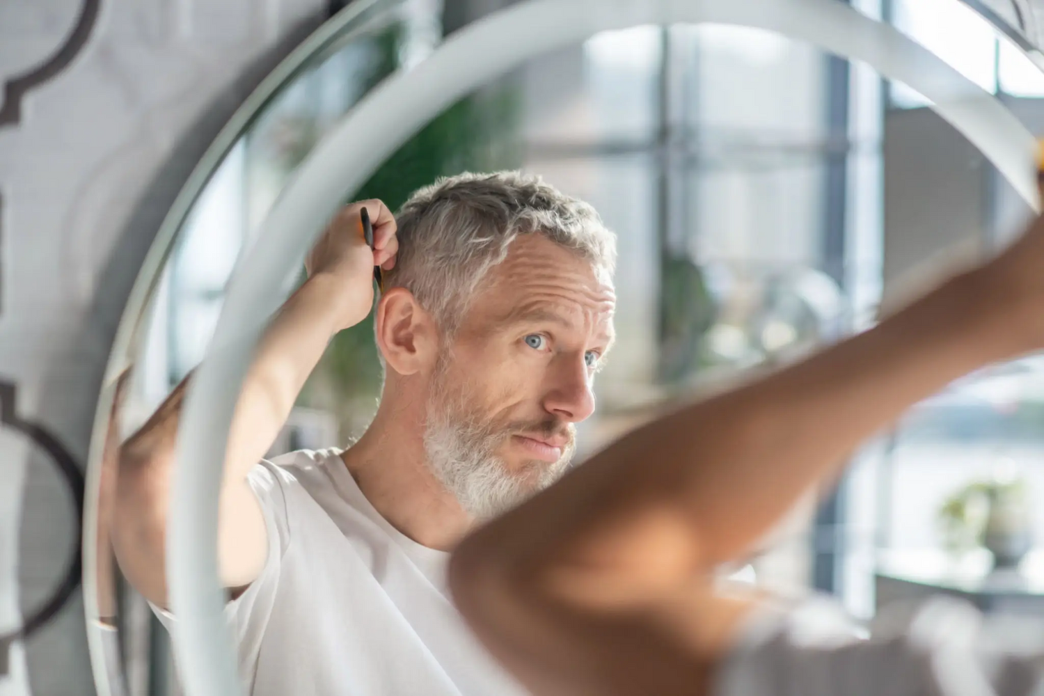 Middle aged man looking worriedly at his thinning hairline in the mirror, highlighting typical hair loss symptoms and underscoring the urgent need for effective treatment like RootRestore’s comprehensive hair restoration protocol with finasteride, dutasteride, and topical minoxidil, proven to help men regain hair thickness and confidence.