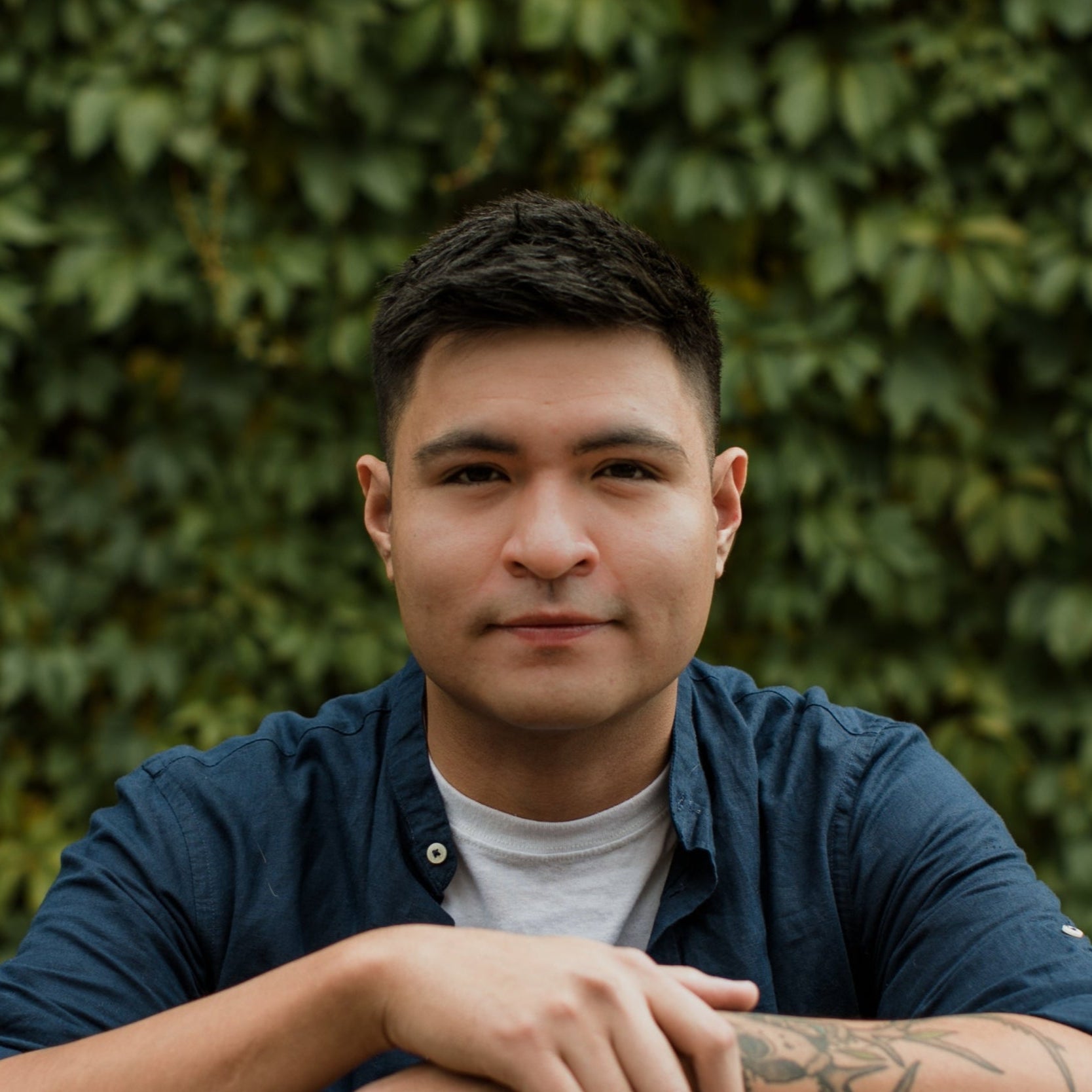 Man wearing a blue shirt with a green leafy background