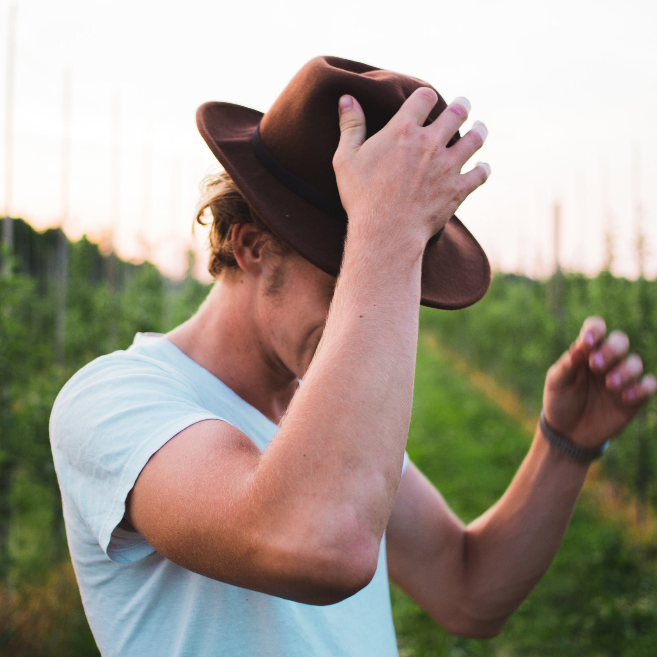 Forty health happy TRT customer testimonial picture adjusting a cowboy hat in an outdoor setting with greenery and a fence for a low T center, men's T clinic, nationally acclaimed leading testosterone replacement institution in USA.