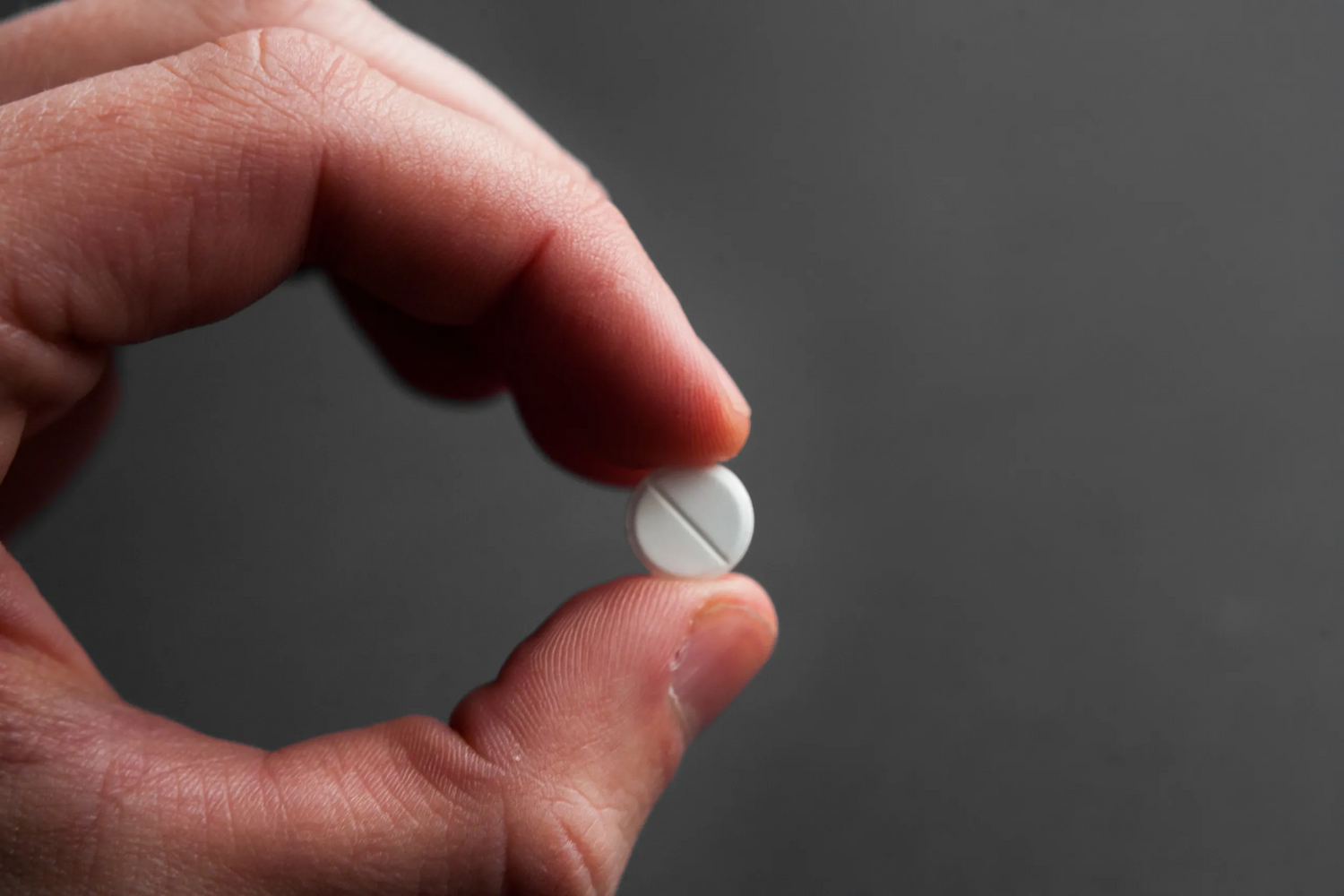 Close-up of a hand holding a white pill against a gray background, representing Forty Health’s premium treatments for hormone optimization, HRT, TRT, GLP-1 weight loss, and men’s wellness.