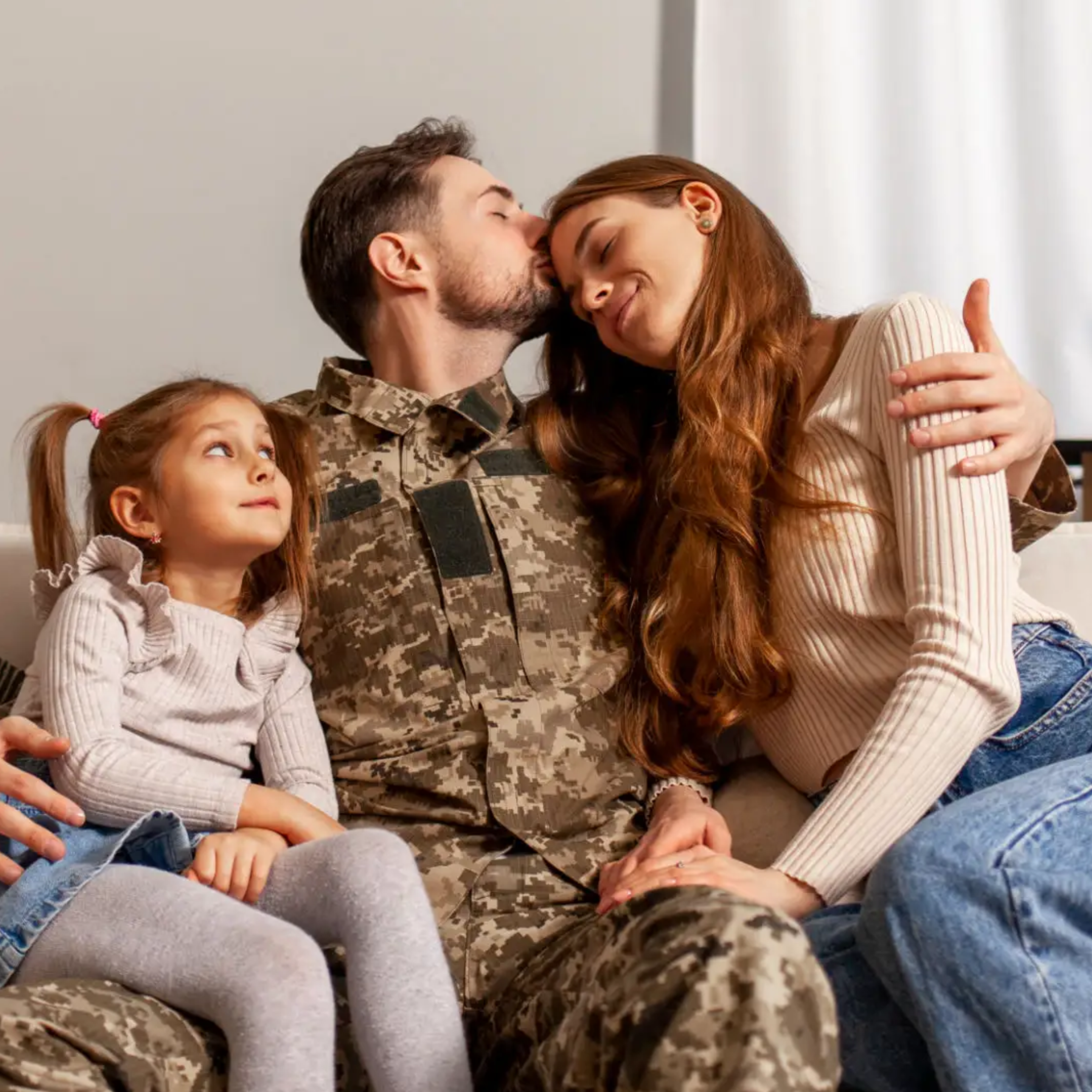 Man in military uniform sitting on a couch with his family, embracing a woman and a young girl showing adoption of military of men's health solutions including TRT, ED medications, hair regrowth, factors that are all affected by high stress and lead towards early death and disability for soldiers. 